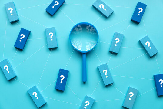 QnA or questions and answers concept. Blue magnifying glass with question symbol on wooden cube over a blue background.