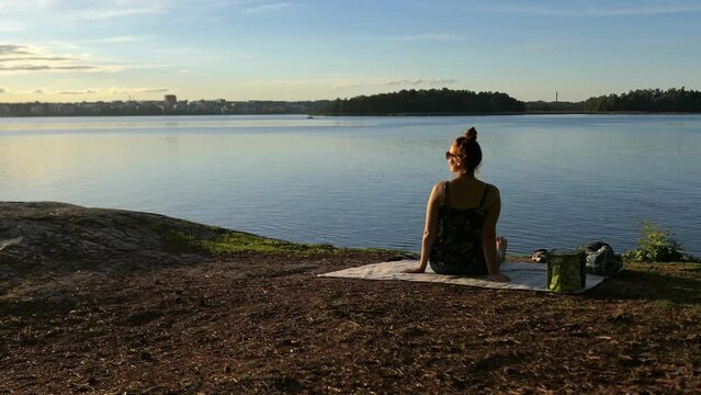 Sunset picnic woman looking at calm sea on rocky shore, rising crane shot