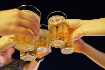 Hands Hold Beverage Beers glass Cheers at the party in the night time. Group of happy friends drinking alcohol at a brewery bar restaurant.
