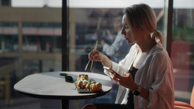 A young woman visits an Asian cafe during lunch, and eats rolls and sushi. Blonde at the table of a stylish cafe.