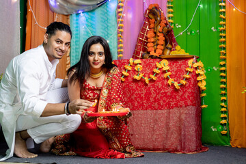 Indian couple decorating home with diya and looking towards the camera ,Festival occasion celebration at home