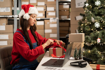 Female online store small business owner seller wrapping gift packing box preparing delivery parcel on table in warehouse. Ecommerce dropshipping sale concept.