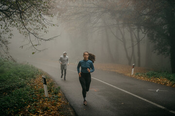 Two runners tackling an uphill path enveloped in fog, symbolizing challenges and determination.