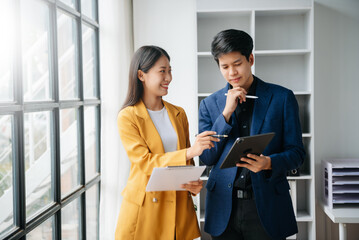 Asian business colleague business presents and explains and using laptop and tablet. Teamwork, financial marketing team,   while sitting in modern office room..