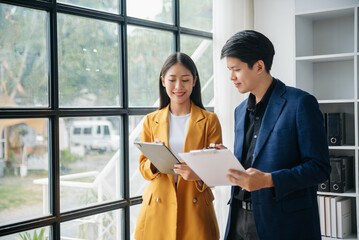 Obraz premium Asian business colleague business presents and explains and using laptop and tablet. Teamwork, financial marketing team, while sitting in modern office room..
