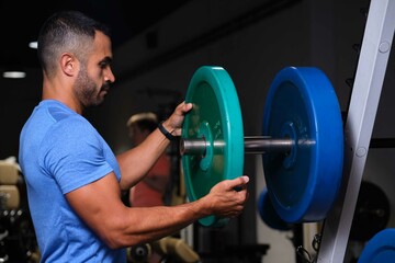 Strong Hispanic man putting weight plate on barbell at a gym.