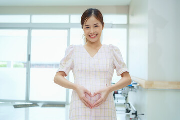Happy and excited pregnant woman making heart shape on her belly at hospital