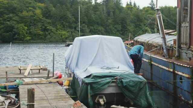 A man mooring a wooden boat with covers to a dock. Timelapse