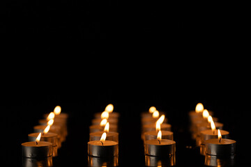 Rows of lit tea candles with copy space on black background