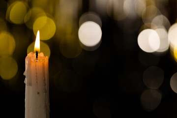 Lit white candle and bokeh with copy space on black background