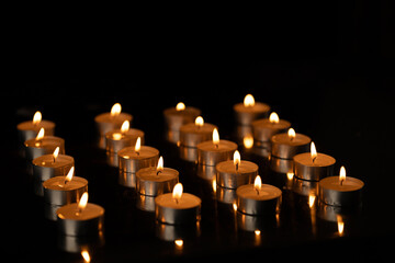 Rows of lit tea candles with copy space on black background