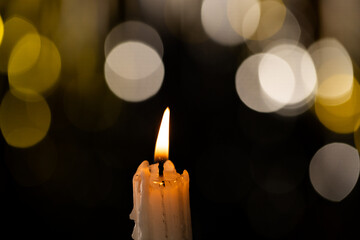 Lit white candle and bokeh with copy space on black background