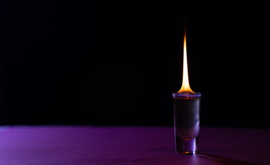 Lit candle in purple glass container with copy space on purple and black background