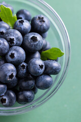 Micro close up of blueberries in glass bowl with copy space on green background