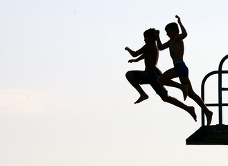 silhouettes of two teenagers jumping together from diving tower to waters of Lake Geneva, Paquis...