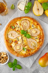 Delicious pizza with pears, gorgonzola cheese, walnuts and basil on a gray concrete background.