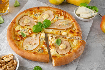Delicious pizza with pears, gorgonzola cheese, walnuts and basil on a gray concrete background.