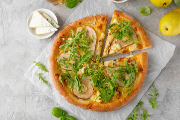 Delicious pizza with pears, gorgonzola cheese, walnuts and arugula on a gray concrete background.