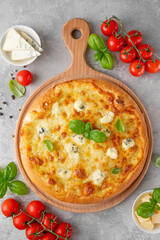 Pizza four cheeses with fresh basil on top on a wooden board on a gray concrete background. Top view, copy space.