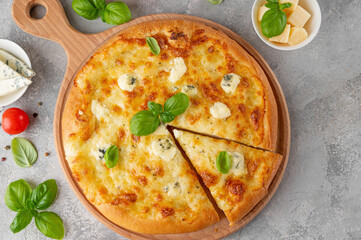 Pizza four cheeses with fresh basil on top on a wooden board on a gray concrete background. Top view, copy space.