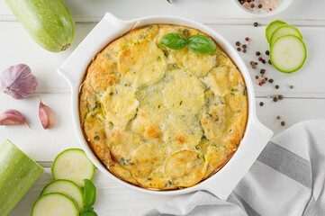 Zucchini casserole in cream cheese sauce in a white baking dish on a white wooden background. Healthy comfort vegetarian food