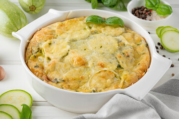Zucchini casserole in cream cheese sauce in a white baking dish on a white wooden background....