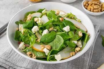 Salad with spinach, arugula, fresh pear, nuts and gorgonzola cheese with olive oil in a bowl. Healthy food concept.