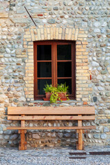 Fototapeta na wymiar Panca in legno davanti a un muro di pietra con finestra con vaso di fiori.