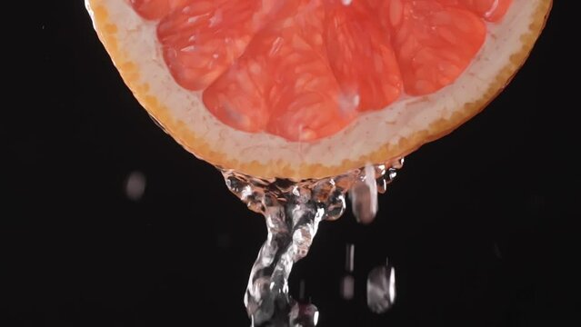 Super slow motion shot of sliced grapefruit slice with splashes of water flying in air on black background. Freshness and refreshing invigorating citrus sough. Lemonade or juice Slow motion. droplets.