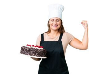 Middle age pastry chef woman holding a big cake over isolated background doing strong gesture