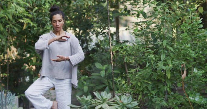 Focused biracial woman practicing yoga in sunny garden, slow motion with copy space