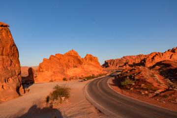 Panoramic sunrise view of endless winding empty road in Valley of Fire State Park leading to red Aztec Sandstone Rock formations and desert vegetation in Mojave desert, Overton, Nevada, USA. Freedom