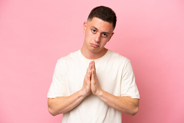 Young Brazilian man isolated on pink background keeps palm together. Person asks for something