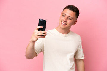 Young Brazilian man isolated on pink background making a selfie