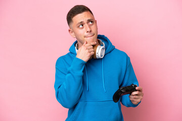 Young brazilian man playing with a video game controller isolated on pink background having doubts...
