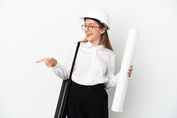 Young architect woman with helmet and holding blueprints isolated on white background pointing finger to the side and presenting a product