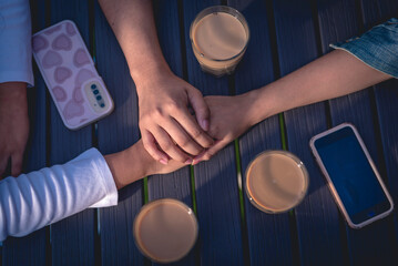 A photo of three hands on top of each other, showing unity, on a table surrounded by coffees and cellphones. A table in the background.