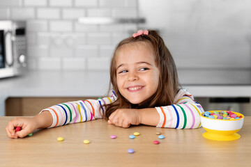 Playful little girl at kitchen table grabbing candies