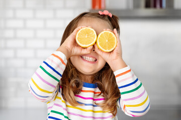 Happy little girl holding lemons against her eyes