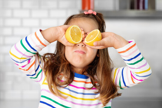 Funny little girl holding lemons against her eyes
