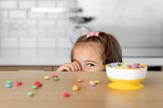 Little girl stealing candies on kitchen table