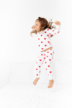 Little girl wearing pajama with printed hearts bouncing on bed