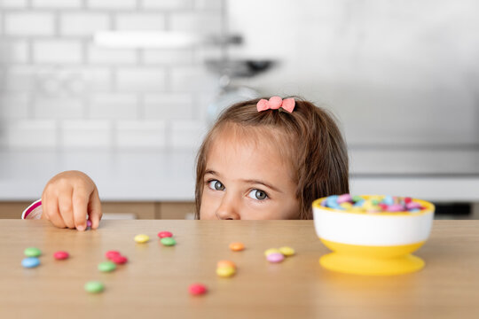 Little girl grabbing candies on kitchen table