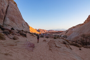 Woman with scenic sunrise view of arid landscape with striated red and white rock formations along the White Domes Hiking Trail in Valley of Fire State Park in Mojave desert, Overton, Nevada, USA