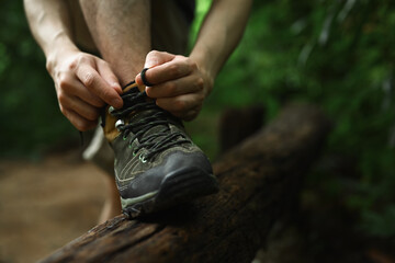 Male hiker tying shoelaces, getting ready walking in forest. Active life, adventure and healthy lifestyle