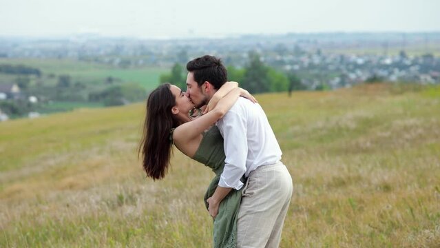 Happy man holds woman in arms on hilly plain standing against blurred city. Concept of posing for photoshoot and young people in relationship slow motion