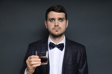 A man in a zombie costume with a drink in his hand on a black background