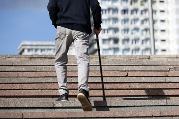 Old man with walking cane climbing stairs on city street. Concept for disability, limping adult