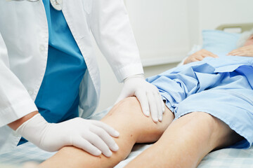 Doctor checking Asian elderly woman patient with scar knee replacement surgery in hospital.