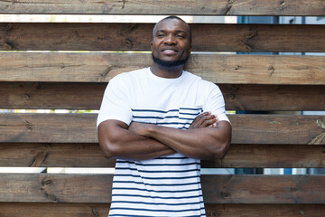 A stylish, young African-American man poses for the camera against the background of a wooden fence